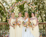 Bride in a white gown holding colorful yellow nad orange florals next to her bridesmaids in yellow dresses