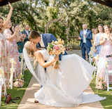 Bride and groom sharing a celebratory kiss during their outdoor wedding ceremony surrounded by guests and peach floral arrangements.