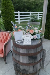 Two multi-color pastel floral vaseless centerpieces sit on top of a wooden barrel next to a vintage phone and signage.