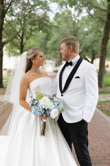 A bride and groom looking at each other while the bride holds a bouquet made of white and blue florals