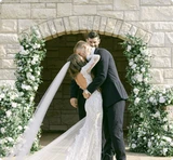 Bride and groom kissing in front of ceremony installation of green and white flowers from the Jane Collection