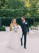 Groom holding brides wedding dress while bride looks at him holding a bouquet made of blue and white flowers