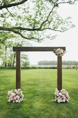 Wooden wedding ceremony arch adorned with a light pink and white floral swag complemented with matching floral meadows at the base of the arch for a minimal wedding ceremony backdrop.