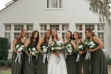 Bride and her bridesmaids wearing  green bridesmaid dresses hold magnolia and camellia floral bouquets with light blue sashes.