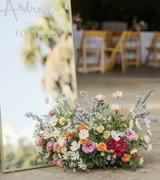 A close-up photo of a multi-color wildflower floral meadow at the base of a mirror welcome sign at a wedding venue.