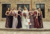 A bride and her bridesmaids wearing different shades of purple pose for a photo holding bouquets made up of florals in different shades of purple.