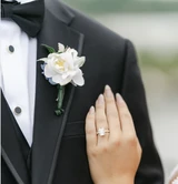 A bride puts her hand on the groom's chest as the pose for a close up of a white rose boutonniere secured to the groom's lapel.