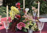 Close up of a large vaseless centerpiece featuring dark red, pink, purple, and green florals