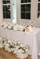 White wedding flower arrangements decorated on a sweetheart table at a wedding reception.