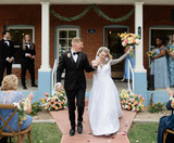 Newlyweds walking down the aisle after their ceremony surrounded by peach floral arrangements and cheering wedding guests.