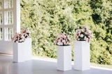 Light pink and ivory floral meadows are placed on top of four white pillars for a minimal wedding ceremony backdrop.