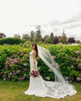 Portrait of a bride in a veil holding a vibrant bouquet of red roses and soft greenery outdoors in front of a hydrangea bush..