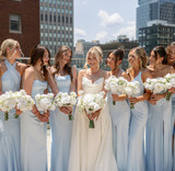 Bride holding white floral bouquet alongside her bridesmaids overlooking a city skyline