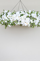 A floral chandelier made of white roses, ranunculus, and orchids, accented with wisteria greenery, suspended from the ceiling