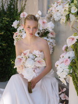 Bride holding wedding bouquet featuring blush pink anthurium, roses, and ivory flowers held in front of a bridal gown.