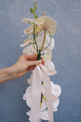The back of a wedding chair decoration featuring blush anthuriums, cascading white orchids, and white ribbon designed for ceremony aisle seating.