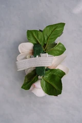 The back of an ivory rose and orchid wrist corsage with greenery, shown as a standalone floral accessory on a grey backdrop.
