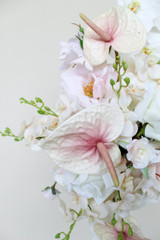 Close-up of a floral arrangement featuring blush anthuriums, white orchids, ivory roses, hydrangeas, and cascading floral accents.