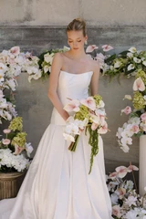 Bride holding a cascading bouquet with blush anthuriums, orchids, hydrangeas, and trailing amaranthus in front of a floral installation.