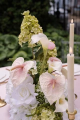 Close-up of a floral arrangement featuring white hydrangeas, blush anthuriums, white orchids, pale pink roses, calla lilies, and soft blush garden roses, styled in the middle of a wedding reception table with gold candlesticks.