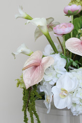 Close-up of a floral arrangement featuring white hydrangeas, blush anthuriums, white orchids, pale pink roses, calla lilies, and soft blush garden roses.