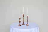 Three copper candlesticks on a white cocktail table in front of a white wall