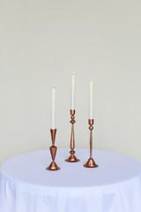 Three copper candlesticks on a white cocktail table in front of a white wall
