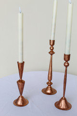 Close up of three copper candlesticks on a white cocktail table in front of a white wall