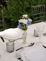 Silver bud vase styled with white and blue florals on a reception table with silverware and cutlery
