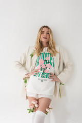 Lifestyle image of a girl wearing the Bouquet Division Tee with a beige blazer standing up against a wall with her hands on her hips