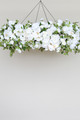A floral chandelier made of white roses, ranunculus, and orchids, accented with wisteria greenery, suspended from the ceiling