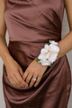 Ivory rose and peach orchid wrist corsage styled on a bridesmaid wearing a satin brown dress.