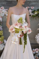 Bride holding a cascading bouquet with blush anthuriums, orchids, hydrangeas, and trailing amaranthus in front of a floral installation.