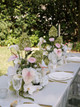 Floral arrangement featuring white hydrangeas, blush anthuriums, white orchids, pale pink roses, calla lilies, and soft blush garden roses, styled in the middle of a wedding reception table with gold candlesticks.