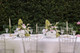 Two floral arrangements featuring white hydrangeas, blush anthuriums, white orchids, pale pink roses, calla lilies, and soft blush garden roses, styled in the middle of a wedding reception table with gold candlesticks.