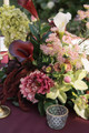 Close up of a faux floral centerpiece featuring deep burgundy and white calla lilies, green cymbidium orchids, pale green hydrangea, blush pink peonies, airy pink astilbe, and cascading burgundy amaranthus arranged on a burgundy linen