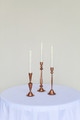 Three copper candlesticks on a white cocktail table in front of a white wall