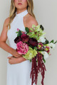 Bride wearing a modern white halter gown holding the Stella Blended Bridal Bouquet, featuring deep burgundy peonies and roses, vibrant pink peonies, white calla lilies, green cymbidium orchids, pale green hydrangea, hellebores, and cascading burgundy amaranthus.