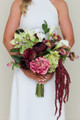 Bride wearing a modern white halter gown holding the Stella Blended Bridal Bouquet, featuring deep burgundy peonies and roses, vibrant pink peonies, white calla lilies, green cymbidium orchids, pale green hydrangea, hellebores, and cascading burgundy amaranthus.