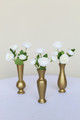 White ranunculus bud vase flowers inside three gold bud vases on a white table in front of a white backdrop