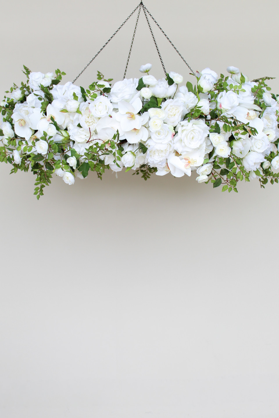 A floral chandelier made of white roses, ranunculus, and orchids, accented with wisteria greenery, suspended from the ceiling