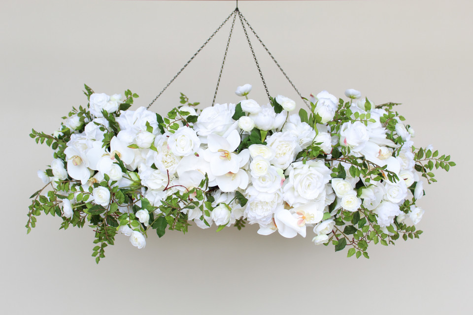 A floral chandelier made of white roses, ranunculus, and orchids, accented with wisteria greenery, suspended from the ceiling