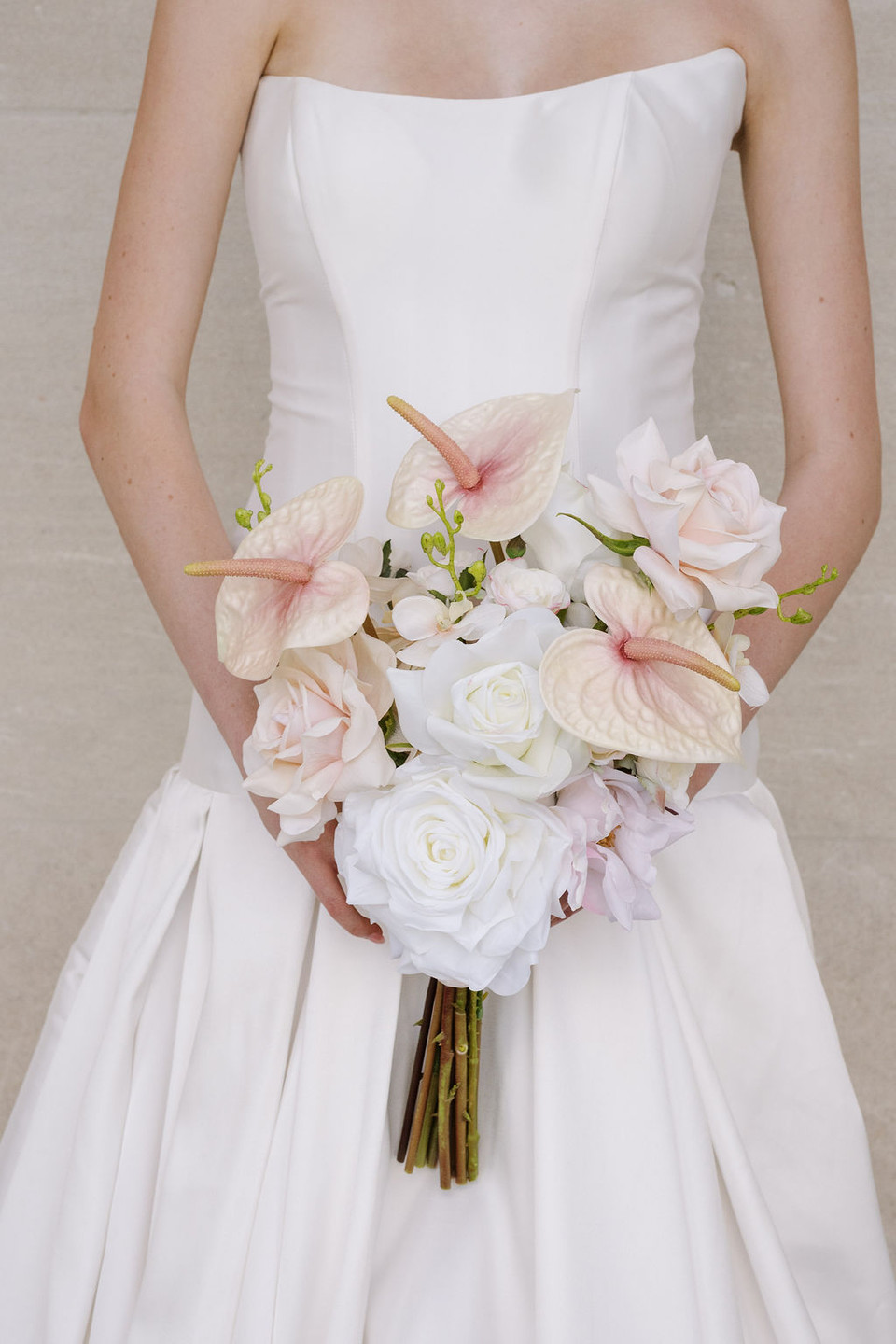 Close-up of a bride in a white gown holding a cascading bouquet of blush pink and ivory flowers.