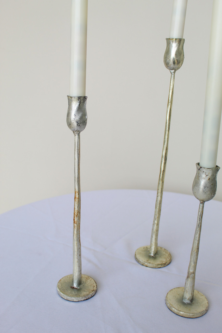 Close-up of three silver candlesticks on a white cocktail table in front of a white wall