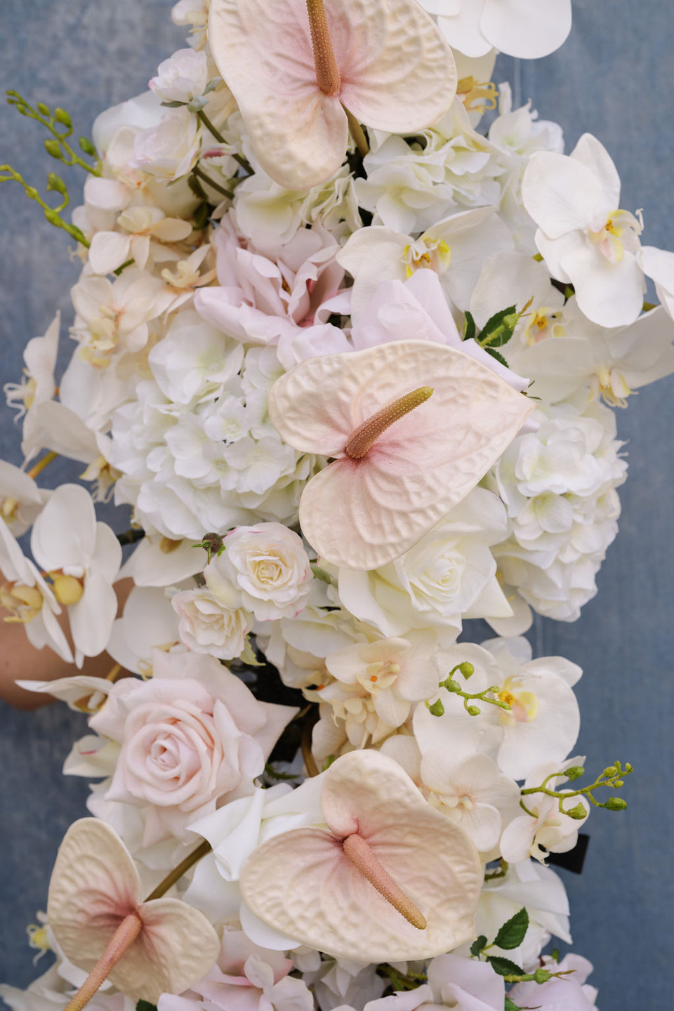 Close-up of a wedding arch arrangement with blush anthuriums, white orchids, hydrangeas, ivory roses, and pastel floral accents.