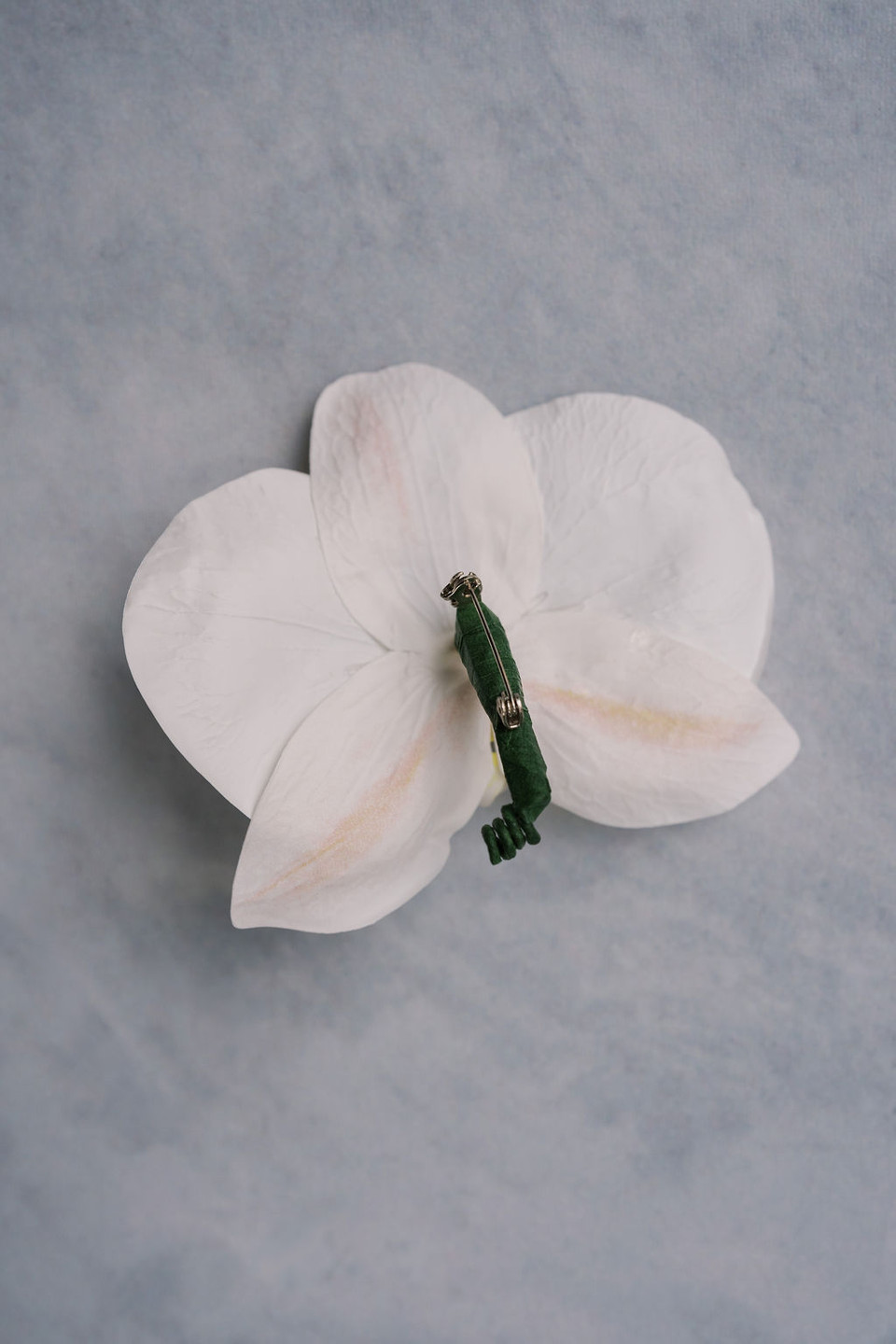 The back of a white orchid boutonniere displayed on a light grey background