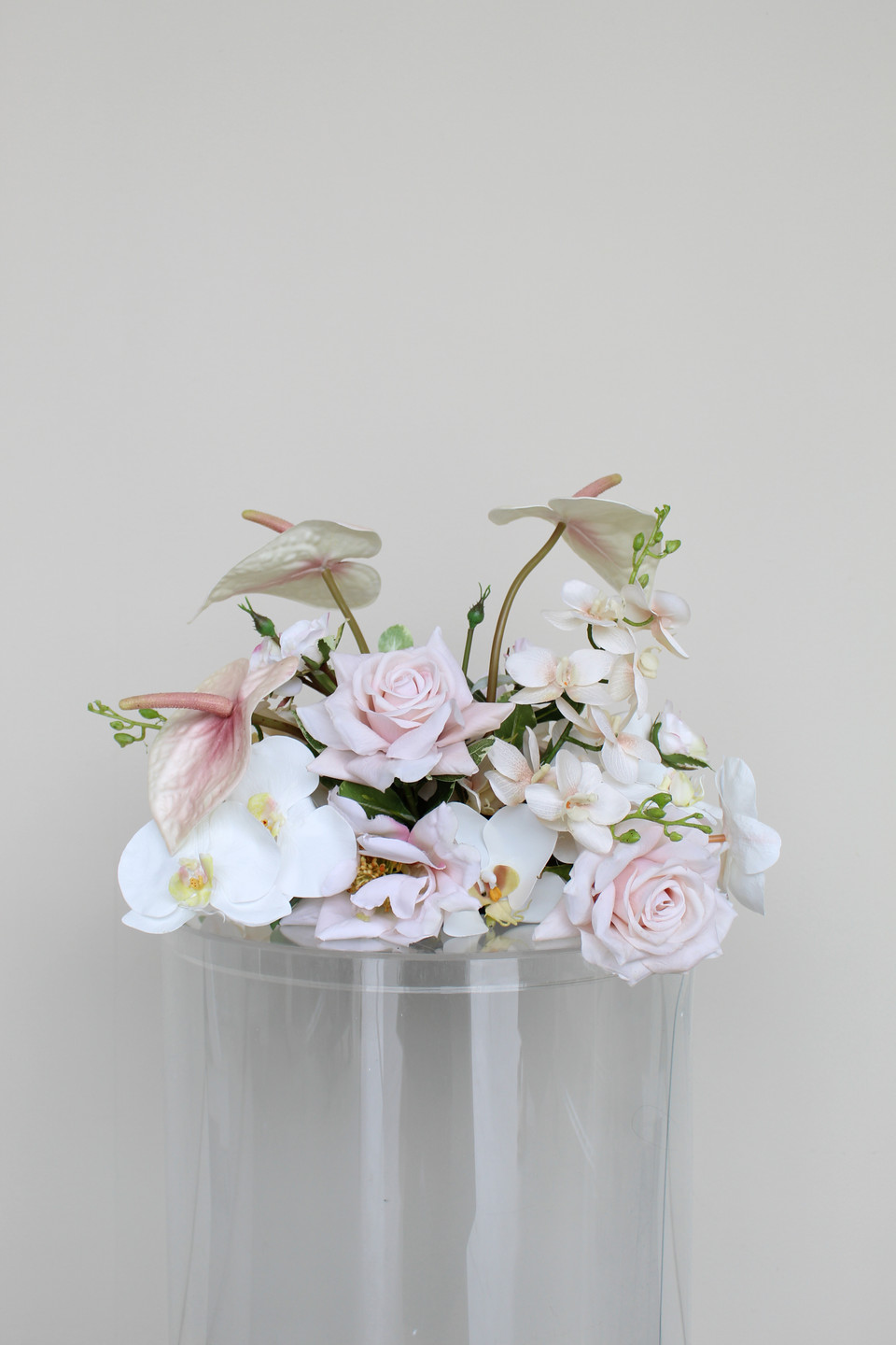 Low floral centerpiece with blush anthuriums, white orchids, pale pink roses, and delicate orchid sprays designed for wedding décor.