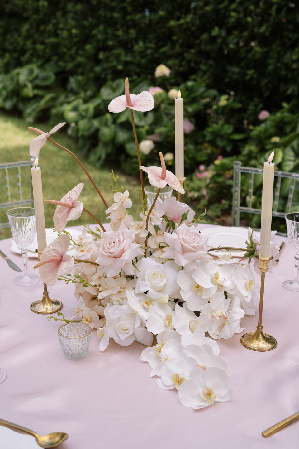Wedding reception centerpiece with blush anthuriums, white orchids, ivory roses, and pale pink roses accented by taper candles.