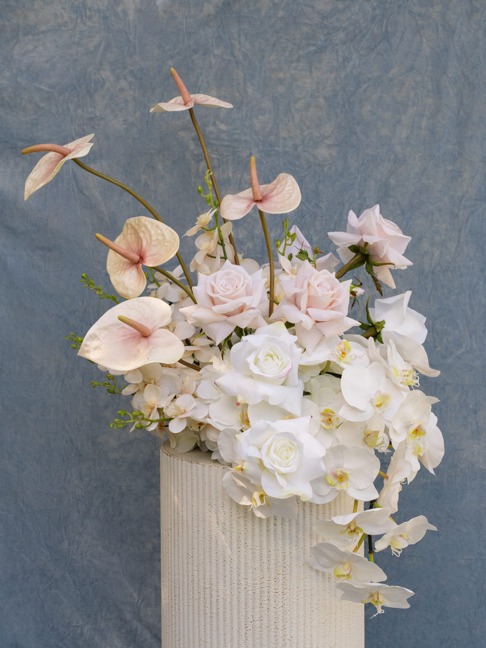 Large vaseless floral arrangement featuring blush anthuriums, white orchids, ivory roses, and pale pink roses in an elevated garden-style design.