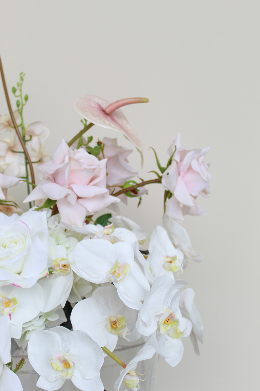 Close-up of large vaseless arrangement with blush anthuriums, white orchids, ivory roses, pale pink roses, and orchid sprays.